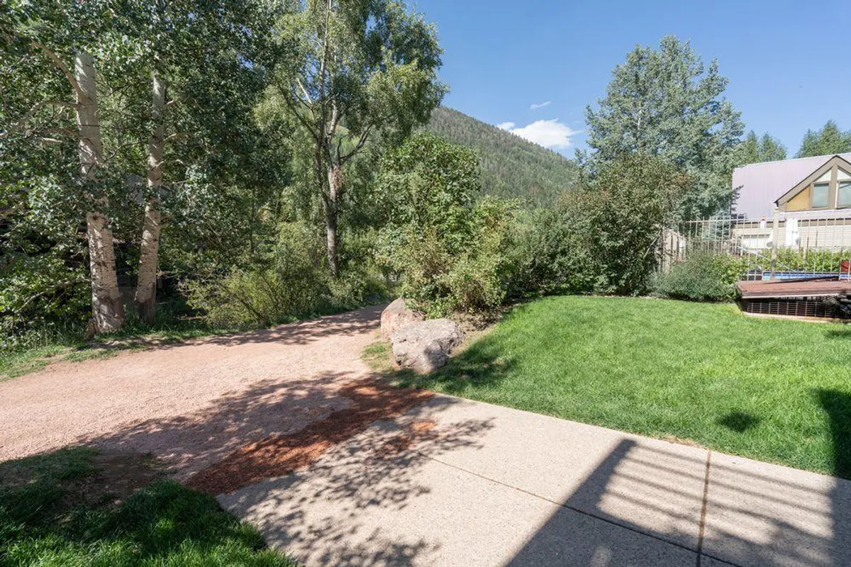 A peaceful grassy area bordered by a winding pathway, lush trees, and a mountain backdrop. The space is ideal for walking, picnicking, or observing nature, with a serene atmosphere that invites families to relax and explore.