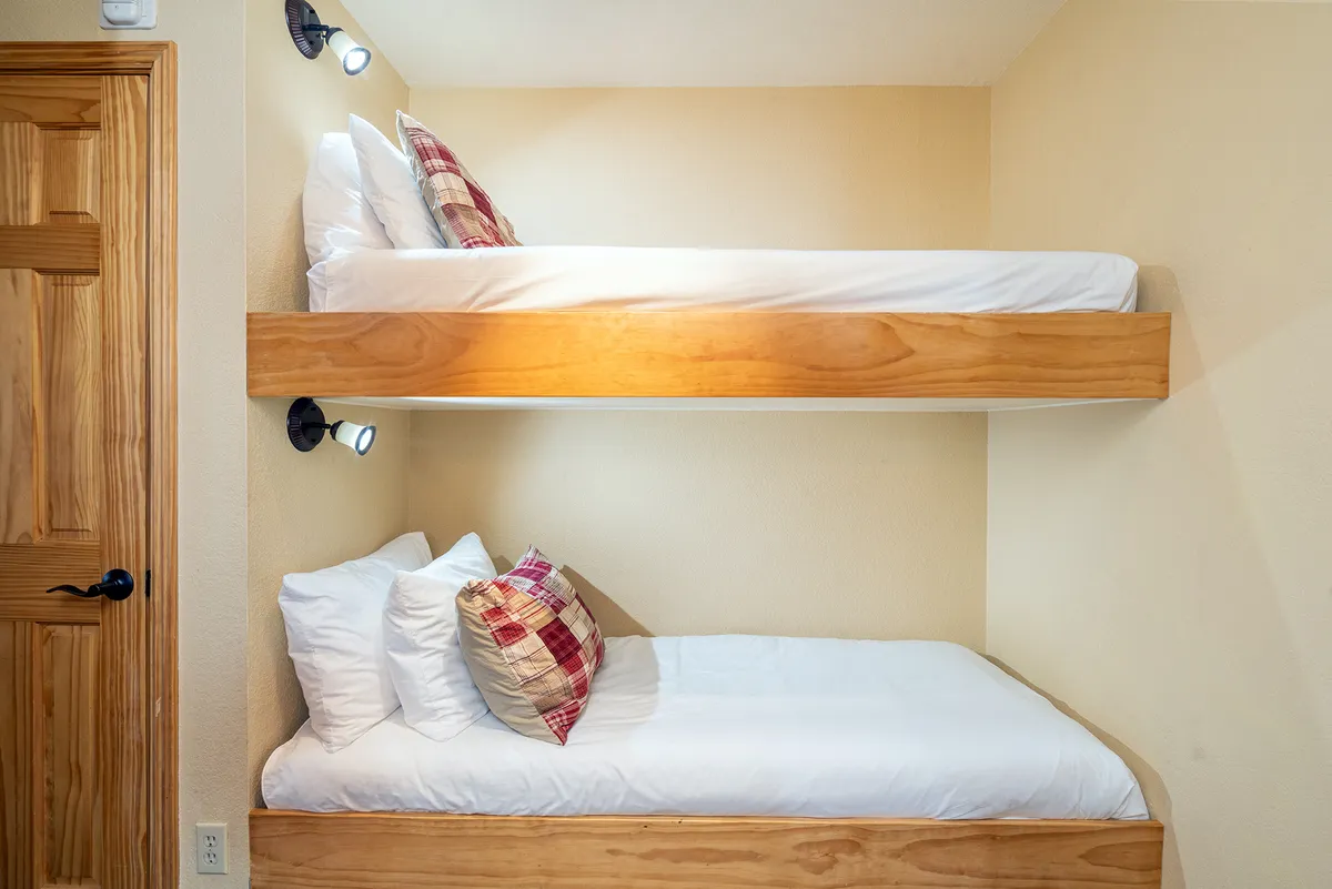 A cozy bunk bed nook with plaid pillows and wooden accents. The space feels intimate and perfect for kids, inviting bedtime stories and sibling laughter.