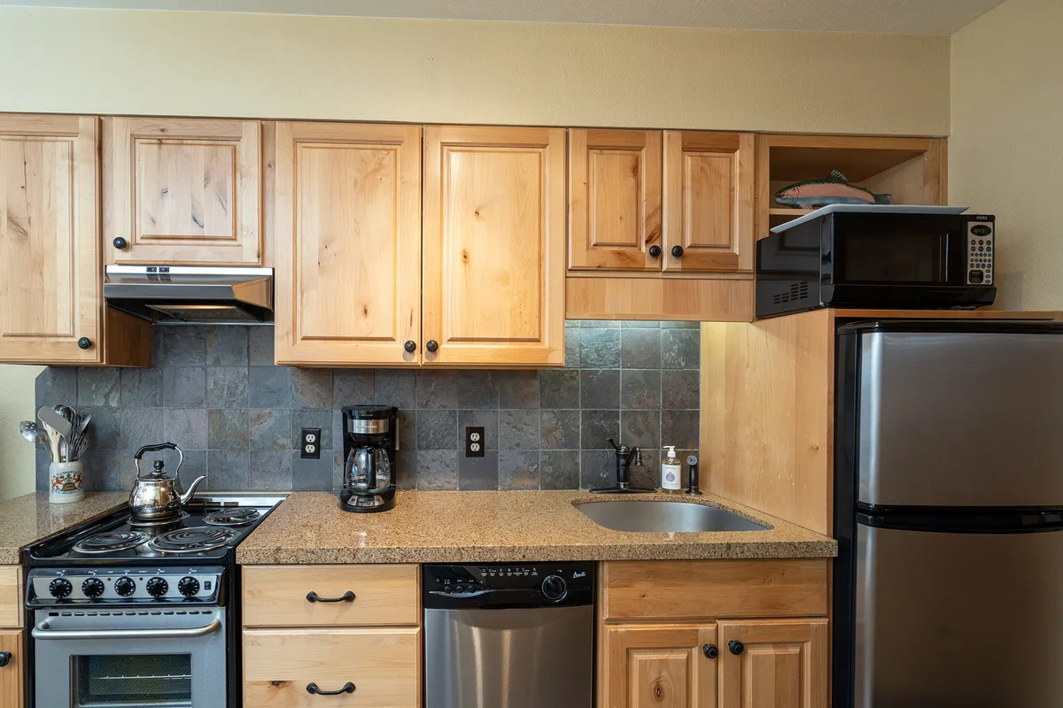 A spacious kitchen featuring warm wooden cabinets, a sleek granite countertop, stainless steel appliances, and stylish tile backsplash. The layout allows for ample cooking and socializing space, creating an inviting environment for meal preparation and gathering.