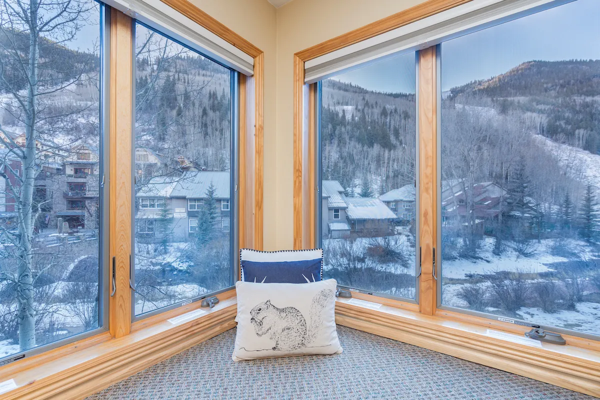 A bright and peaceful seating nook by large windows, offering cozy cushions and uninterrupted views of the river and mountains outside. Natural light fills the area, creating a perfect spot for reading or enjoying coffee while admiring the scenery.
