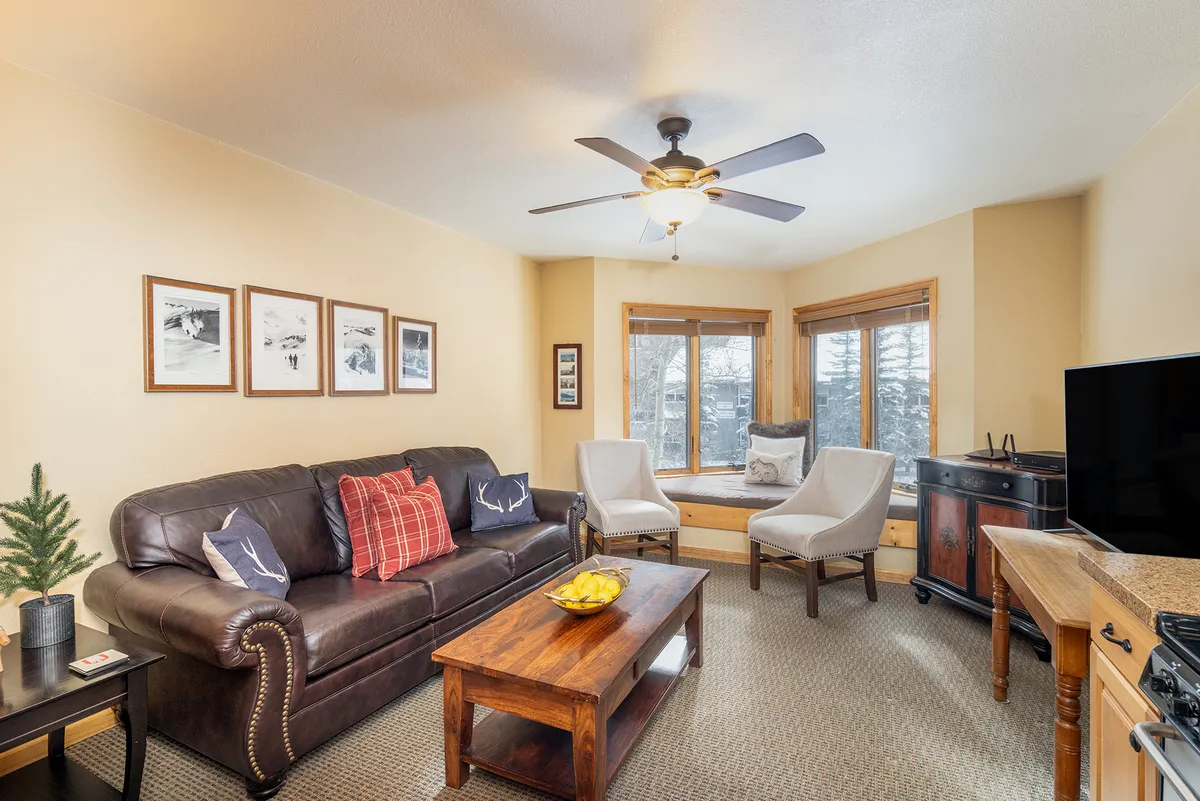 A warm and inviting living space furnished with a leather sofa, wooden coffee table, and window seating. Framed photographs add a personal touch, while ample natural light makes the room welcoming. This central gathering space encourages relaxation, socializing, and staying connected—perfect for families or couples.