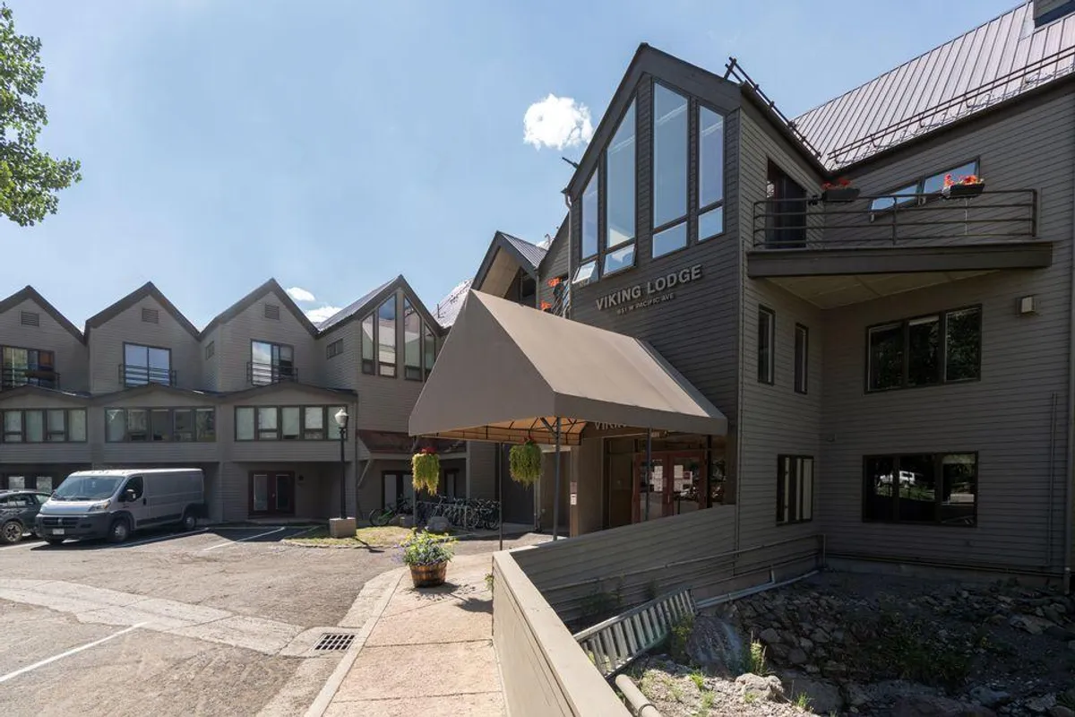 The welcoming Viking Lodge entrance with a prominent sign, entrance awning, large windows, and glimpses of other surrounding buildings. The scene conveys an inviting arrival point and hints at the lodge's proximity to local attractions.